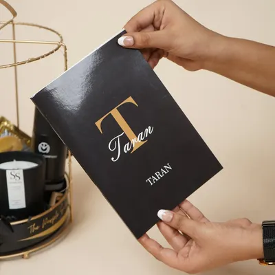 A personalized notebook for "Taran," part of a birthday hamper for him. The elegant monogram adds a sophisticated, custom touch.