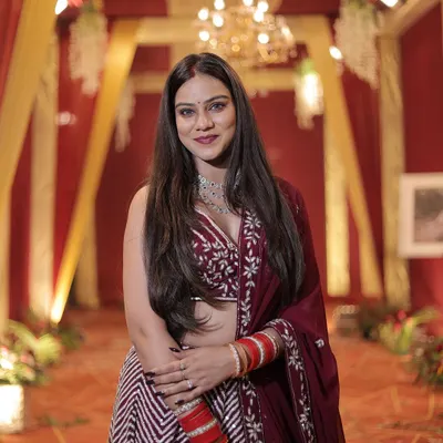 A happy client looking radiant in a maroon and white chevron pattern lehenga at a wedding reception. The outfit is paired with a modern diamond necklace.
