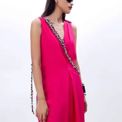 A silhouette that whispers elegance. A model in a vibrant fuchsia draped dress with a beautifully embellished strap detail.