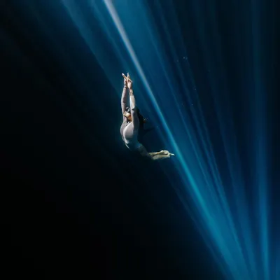 A freediver performs a graceful ascent, framed by dramatic light rays in a cenote. This shot is a perfect example of the collaborative and artistic nature of underwater portrait photography.