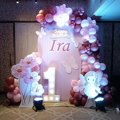A beautiful fairy-themed first birthday for baby Ira. This setup includes a custom pink backdrop, a marquee number '1', a fairy cutout, and an organic balloon garland in shades of pink and purple.