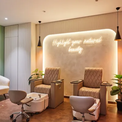 The pedicure station at HQ Smart Salons, designed for ultimate comfort. The combination of plush seating, warm ambient lighting from the neon sign, and gentle pendant lights creates a tranquil and luxurious atmosphere.