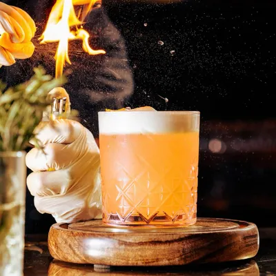 Great cocktails are about blending beautiful presentation and exquisite taste. Here, our mixologist adds a flaming citrus peel to a classic cocktail, creating a spectacle of flavor and aroma.