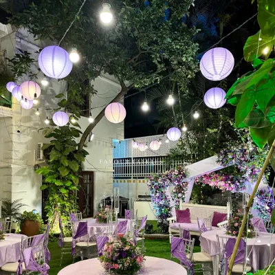 An enchanted evening under the stars. This garden party setup features a purple and lavender color scheme, with paper lanterns and string lights creating a magical canopy.