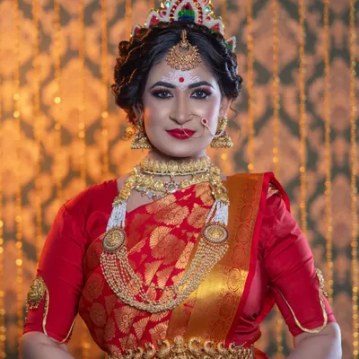 A classic Bengali bride, complete with the traditional 'Mukut' (crown), intricate white and red bindi design, and bold, kohl-rimmed eyes. The red Banarasi saree and gold jewellery complete this timeless look.