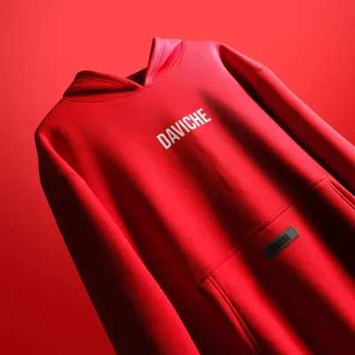 A professionally styled product shot of a red "Daviche" hoodie against a matching red background. The dramatic lighting creates sharp folds and highlights the texture of the fabric.
