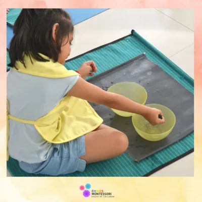 A child engages in a water-based practical life activity, learning control and precision while enjoying the sensory experience.