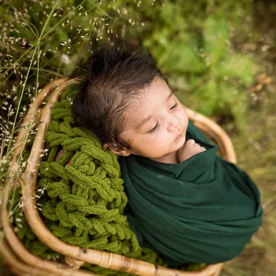 A newborn rests peacefully in a wicker basket, nestled in soft green wraps. This outdoor shot combines my love for nature with the delicate beauty of a new baby.