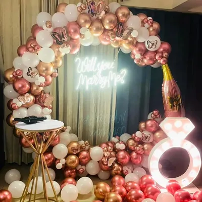 The perfect setup for a romantic proposal. This circular arch of rose gold and white balloons, complete with a 'Will you Marry Me?' neon sign and a light-up ring prop, creates a beautiful and memorable moment.