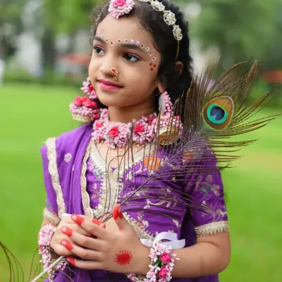 A stunning portrait of a young girl dressed as Radha, holding a peacock feather. The details, from the floral jewelry to the traditional purple attire, are captured beautifully.