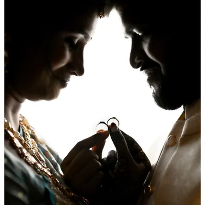 A silhouette of the couple holding their rings together against a bright background. This artistic shot creates a powerful and intimate image focused solely on their commitment.