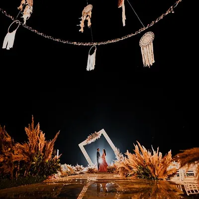 A breathtaking engagement setup under the stars. The couple is framed by a beautiful floral arch, surrounded by pampas grass and dreamcatchers, creating a truly magical "she said yes" moment.