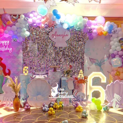 A stunning, wide view of our "Mermazing" celebration. This setup features multiple backdrops, a shimmering silver curtain, and an array of underwater props like shells, coral, and a light-up number '6'.