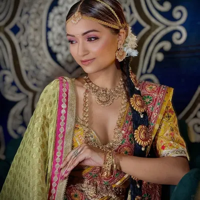 A beautiful South Indian bridal look, showcasing the traditional Kanjeevaram saree and temple jewelry. The makeup features warm tones and a classic braided hairstyle.