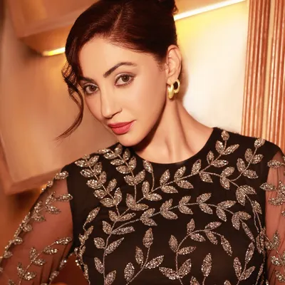 A portrait of actress Reyhna Pandit, capturing her elegance in an intricately embroidered black dress. The warm lighting and intimate setting create a timeless, sophisticated mood.