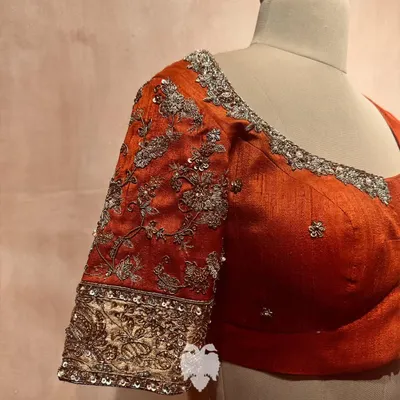 A close-up of a rust orange raw silk sleeve, adorned with delicate floral embroidery in zardosi, zari, and beads.