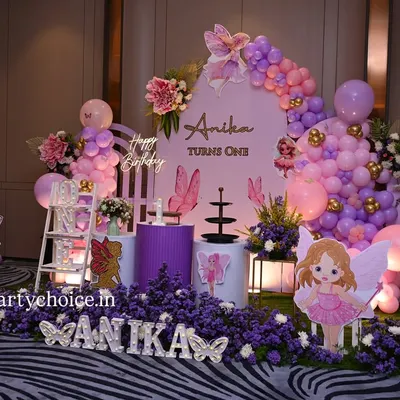 A stunning butterfly and fairy theme for a first birthday. This enchanting setup features a field of purple flowers, fairy and butterfly cutouts, a personalized backdrop, and beautiful pink and purple balloon arrangements.