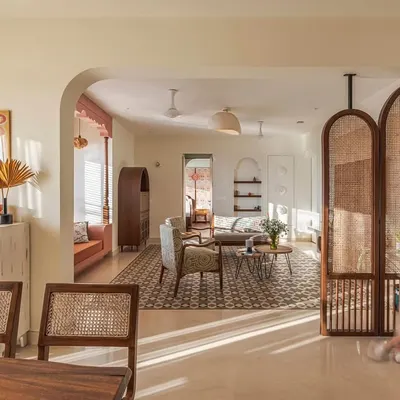 This living room is the heart of a home designed for tranquility. Sunlight streams in, highlighting the geometric floor tiles and the rich textures of the wooden furniture. A custom cane partition offers a glimpse into the dining area, creating an open yet intimate feel.