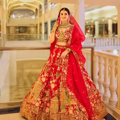 A full-length shot of the bride in a magnificent red lehenga, taken at the Omaxe Chowk. The grand, well-lit architecture of the location provides a stunning backdrop that enhances the regality of the bridal attire.