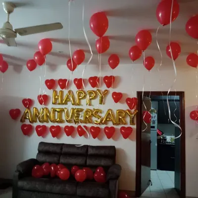 A classic happy anniversary room decoration with red heart-shaped balloons and gold foil letters on the wall.