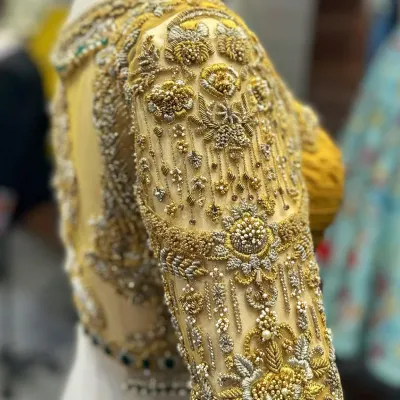 A detailed close-up of a sleeve from our gold bridal blouse. You can see the incredible density of the zardosi, beadwork, and threadwork, creating a rich, three-dimensional texture that is pure luxury.