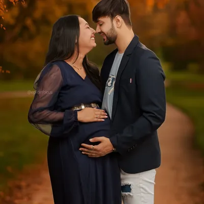 An intimate moment between partners in a beautiful autumn park setting. This couple's maternity photo highlights the warmth and connection as they await their baby.