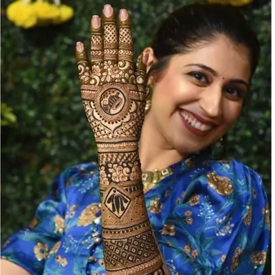 A happy bride showing off her personalized mehndi, which features a dhol and kalash, celebrating her culture.