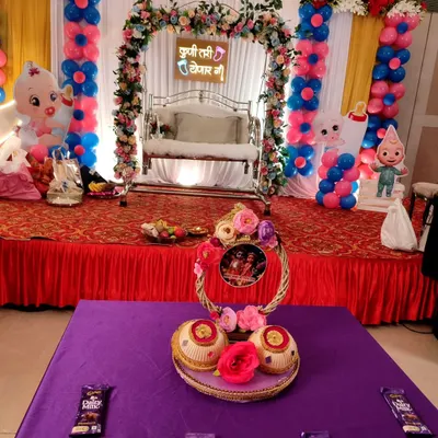 A beautiful stage setup for a traditional baby shower, complete with a decorated swing for the mom-to-be and festive pink and blue balloon columns.