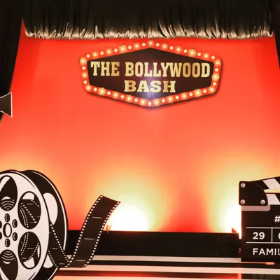 The main backdrop for 'The Bollywood Bash,' a get-together event for Fern Hotels & Resorts. The design features a classic cinema marquee sign against a vibrant red curtain, setting the perfect tone for a film-themed party.
