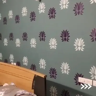 This bedroom accent wall features a beautiful two-tone lotus flower stencil. This technique is perfect for adding a touch of elegance and pattern to a room, creating a custom wallpaper effect with paint.