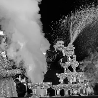 Kishan pops a bottle of champagne, creating a celebratory fountain. This black and white shot captures the energy and excitement of a wedding party, freezing the explosion of joy in time.