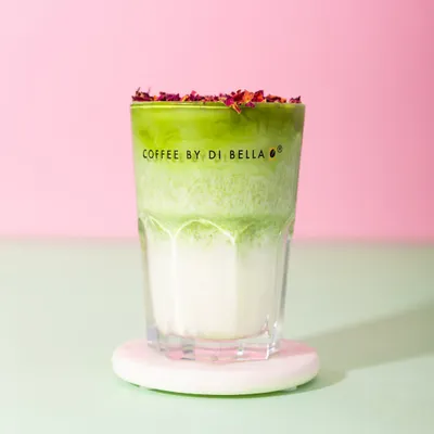 A vibrant Rose Matcha Latte from Coffee By Di Bella. The distinct layers of green and white, topped with rose petals, create a beautiful and Instagrammable image against a colorful background.