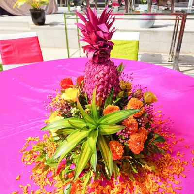A unique and vibrant centerpiece perfect for a Haldi or tropical-themed event. We used a painted pink pineapple surrounded by bright orange marigolds and lush green leaves to create a fun and festive table decoration.