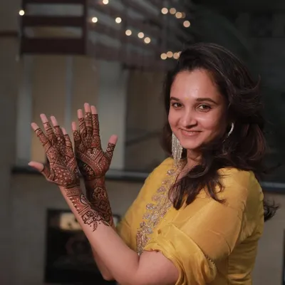 A happy guest showing off her party mehendi against a backdrop of festive lights.