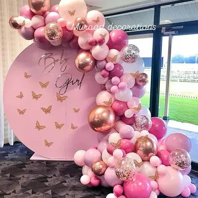 A beautiful 'Baby Girl' announcement setup for a baby shower. The design features a pink circular backdrop with butterfly decals, framed by a stunning balloon garland in shades of pink, rose gold, and confetti.