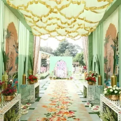 An elaborate entrance for a Pichwai-themed Mehendi. This setup features a custom-printed floral walkway, pastel green drapes with traditional motifs, and an ornate ceiling treatment, leading to the main event area.