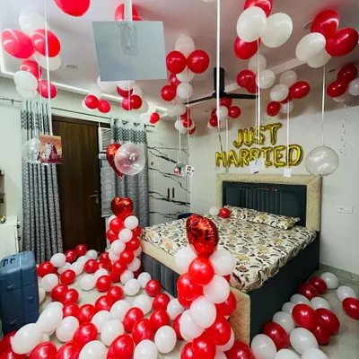 A classic "Just Married" bedroom decoration. The room is filled with red and white balloons on the floor and ceiling, with foil letters above the bed and personalized photos hanging from ribbons for a sweet, memorable touch.