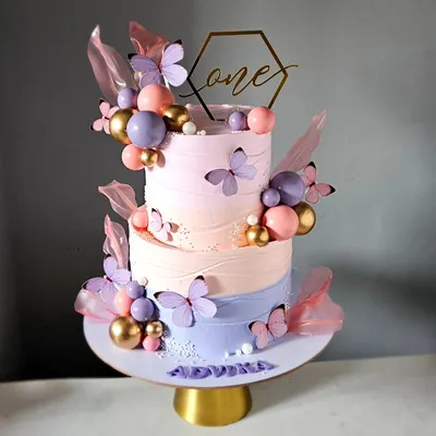 A dreamy, three-tiered butterfly cake in soft pastel shades of pink, peach, and lavender. This design features delicate rice paper sails and a cascade of butterflies, creating a "so pinteresty" look for a first birthday.