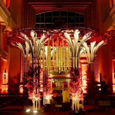 A breathtaking entrance for a grand reception, featuring a massive, sculptural structure adorned with red flowers and hanging golden strings, all lit to perfection.
