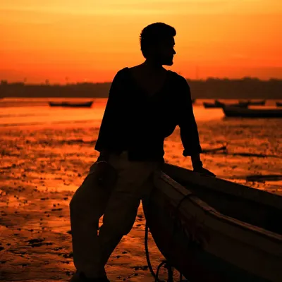 A classic silhouette shot against a fiery orange sunset on the beach. This dramatic lighting is perfect for creating moody and artistic portraits for a male model's portfolio.