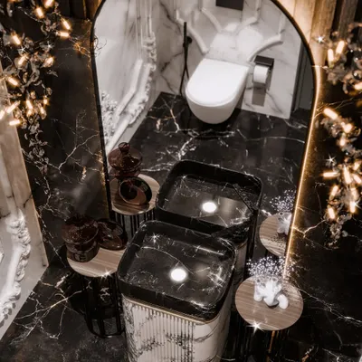 A top-down view of a dramatic powder room, showcasing the contrast between the black marble floor and the monolithic white marble pedestal sink. The render captures the glow of the sculptural lights.