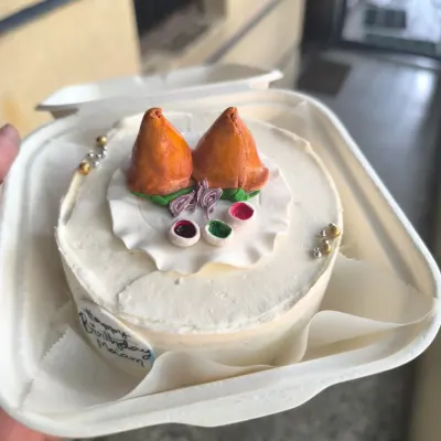 This custom samosa-themed bento cake is a perfect example of how we can turn any inside joke or craving into a sweet celebration. It features two fondant samosas complete with edible chutney, all packed in a convenient takeaway box.