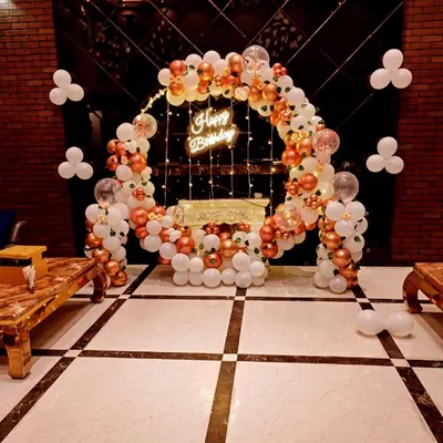A beautiful birthday ring decoration with white and rose gold balloons, a neon sign, and fairy lights, creating an elegant photo spot.
