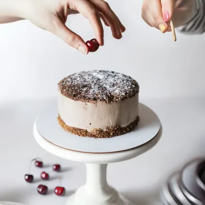 A behind-the-scenes look at the art of food styling, with hands carefully placing a cherry on a chocolate cake. This type of shot tells a story of craftsmanship and fresh ingredients.