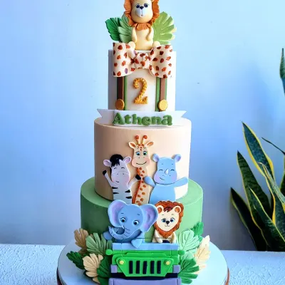 This three-tier safari cake is a fun and detailed creation for a child's birthday. It features multiple fondant animals like a lion, elephant, and zebra, with a cute bow and jeep accent, making it a vibrant centerpiece for a jungle-themed party.