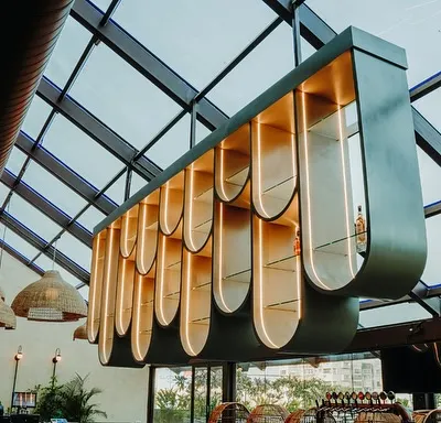 The centerpiece of this resto-bar is the sculptural, suspended bar display, which adds drama and artistry to the space, especially under the glass ceiling.