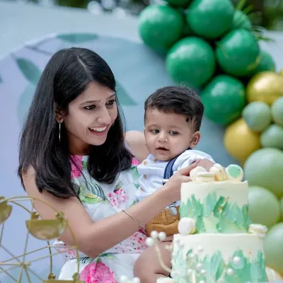 Celebrating a year of giggles and love! A mother helps her baby with his beautiful first birthday cake, surrounded by festive decorations.