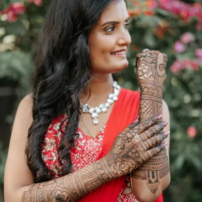 A radiant bride-to-be, her smile as bright as her red lehenga, showing off her intricate bridal mehendi.