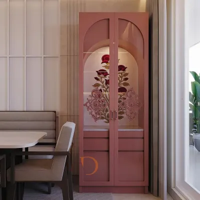 An elegant crockery unit in a soft pink finish, featuring arched glass doors with intricate floral artwork, perfectly integrated into a dining space.