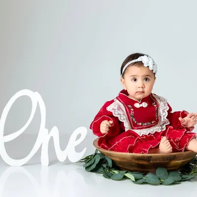 A simple and elegant portrait session featuring a beautiful red dress and a classic 'One' sign to mark the special milestone.